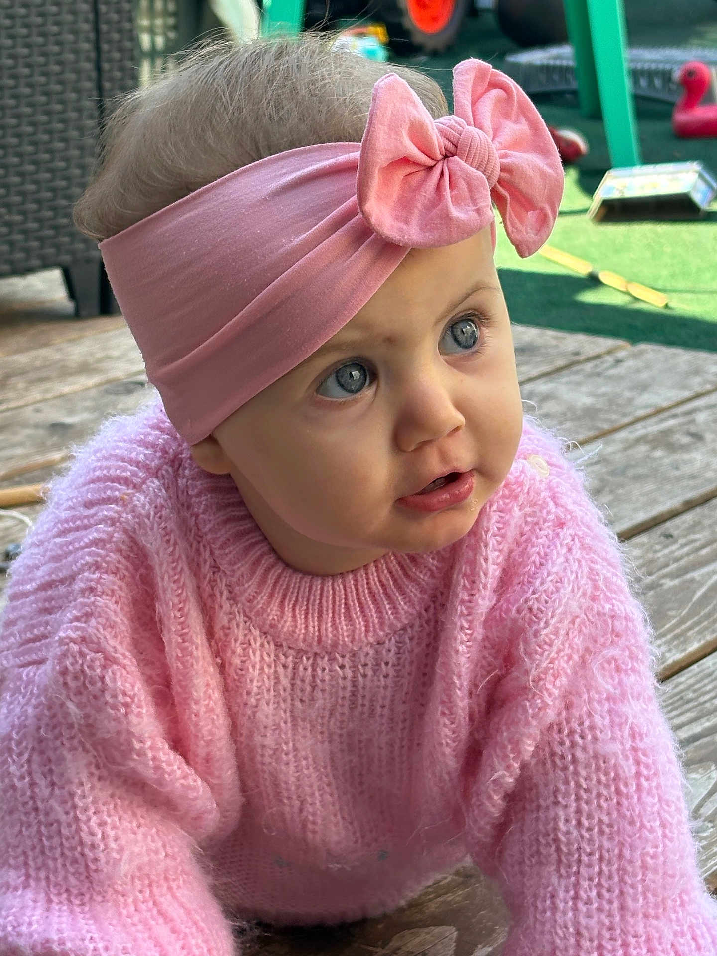Ava a rejoint le concours — aidez-le/la à gagner de superbes lots ! baby, child, pink_sweater, headband, bow, blue_eyes, outdoor, wooden_deck, toy, curious, crawling, knitwear, portrait, closeup, infant, face, person, casual, cute, daylight