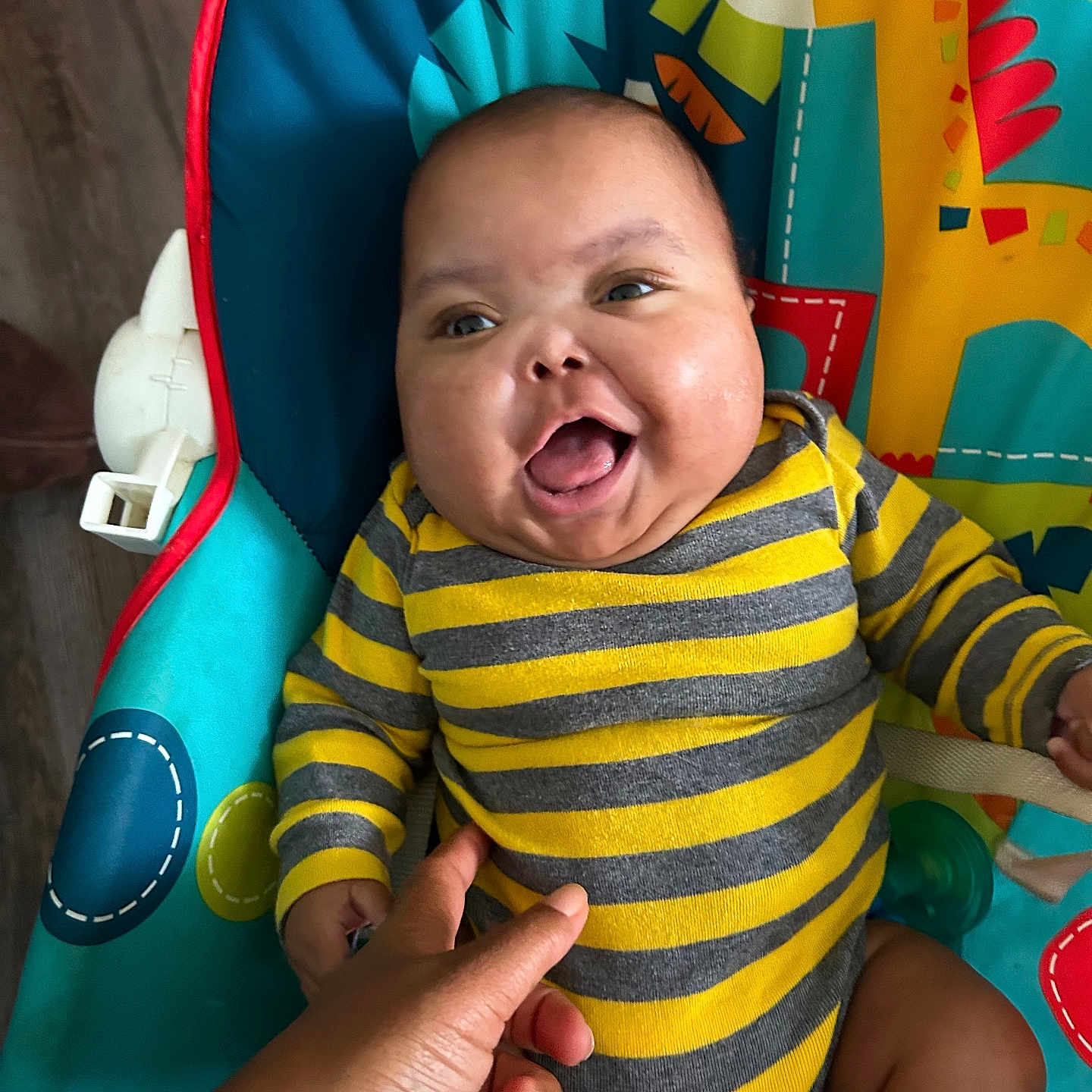 Jhakari is registered to the contest to win money with this photo: baby, baby_chair, cheerful, child, colorful, cute, giraffe_pattern, hand, happy, indoors, infant, onesie, person, playful, portrait, seat, smiling, striped_clothing, toddler, toy