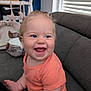 Lise a rejoint le concours — aidez-le/la à gagner de superbes lots ! baby, child, smiling, happy, blue_eyes, orange_shirt, couch, indoors, cute, infant, foot, hair, face, person, home, soft_toys, furniture, window, natural_light, seated