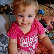 Royal is registered to the contest to win money with this photo: baby, child, infant, sitting, portrait, smiling, blue_eyes, pink_shirt, floral_pants, bed, bedroom, plush_toy, cow_toy, adult, bracelet, indoor, home, close_up, casual_photo, happy