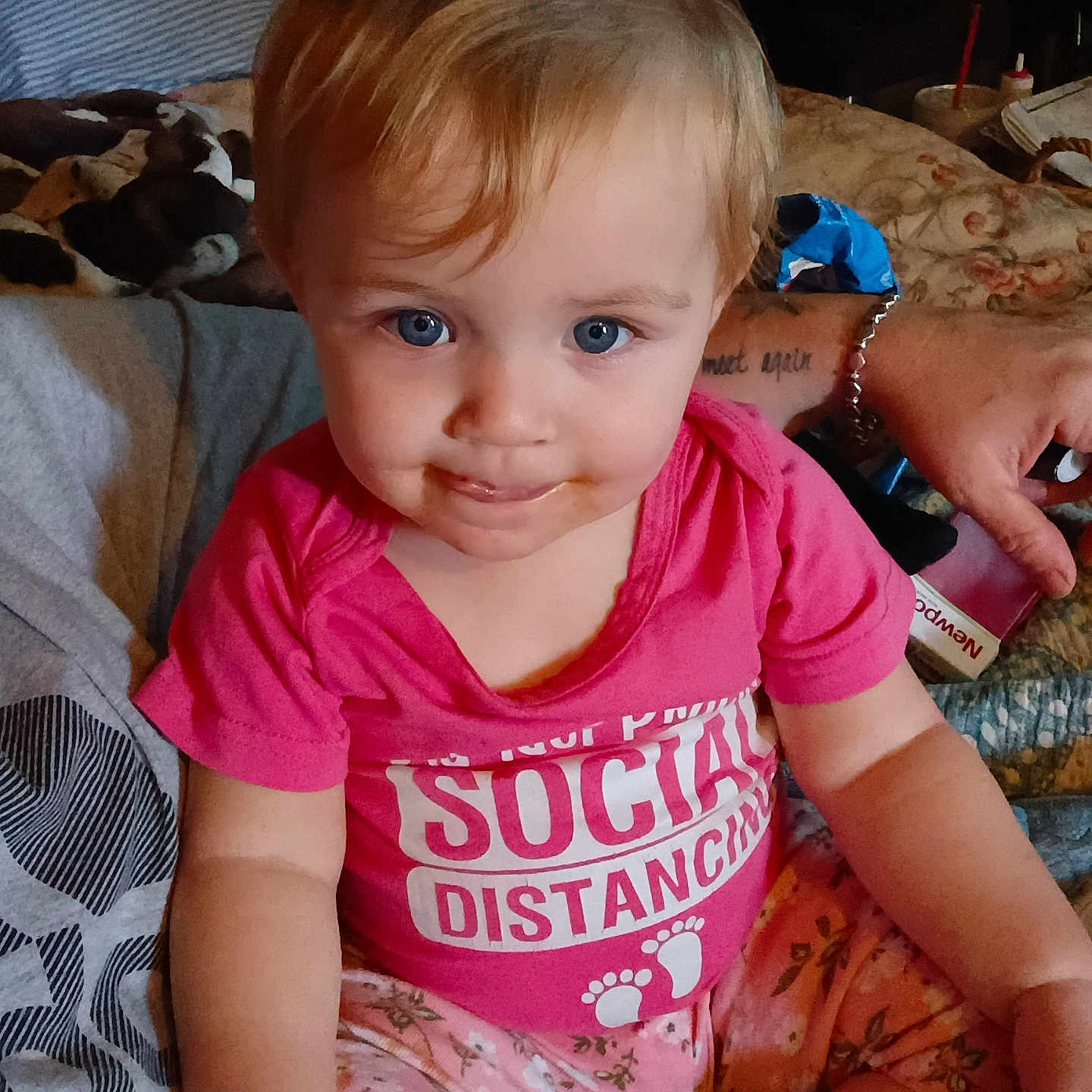 Royal is registered to the contest to win money with this photo: baby, child, infant, sitting, portrait, smiling, blue_eyes, pink_shirt, floral_pants, bed, bedroom, plush_toy, cow_toy, adult, bracelet, indoor, home, close_up, casual_photo, happy