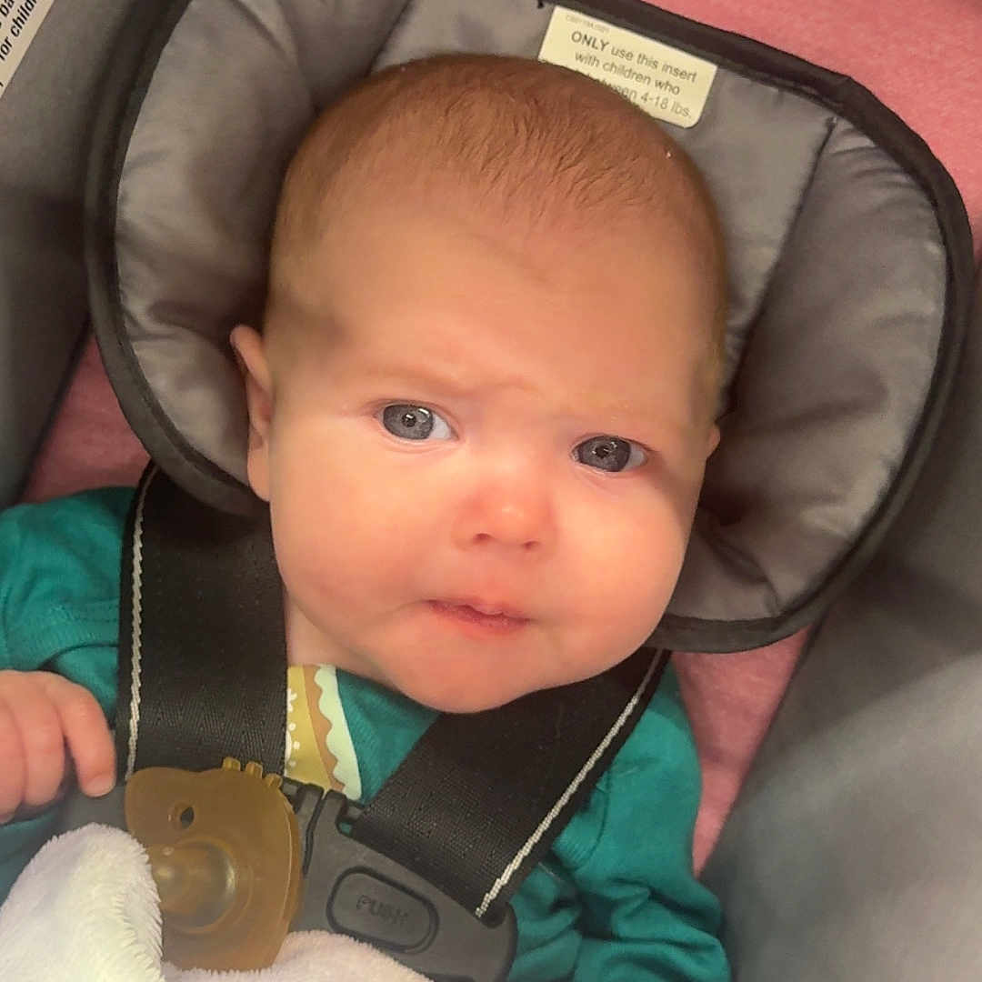 Lila joined the competition — help win amazing prizes! baby, blanket, blue_eyes, car_seat, child, closeup, clothing, cute, expression, gray, hand, head_support, indoors, infant, pacifier, person, pink, seat_belt, soft, straps