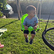 Nolan participe au concours pour gagner de l'argent avec cette photo : toddler, child, swing, pacifier, green_swing, outdoor, grass, playground, summer, daylight, sandals, shirt, cartoon_clothing, fence, toy, play, young_child, park, sunlight, recreation
