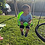 toddler, child, swing, pacifier, green_swing, outdoor, grass, playground, summer, daylight, sandals, shirt, cartoon_clothing, fence, toy, play, young_child, park, sunlight, recreation