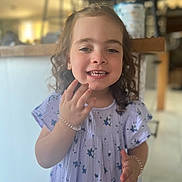 Emy participe au concours pour gagner de l'argent avec cette photo : child, girl, smiling, curly_hair, dress, floral_pattern, bracelet, earrings, indoor, kitchen, counter, blurred_background, happy, portrait, person, young, cute, hand, standing, casual