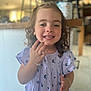 child, girl, smiling, curly_hair, dress, floral_pattern, bracelet, earrings, indoor, kitchen, counter, blurred_background, happy, portrait, person, young, cute, hand, standing, casual