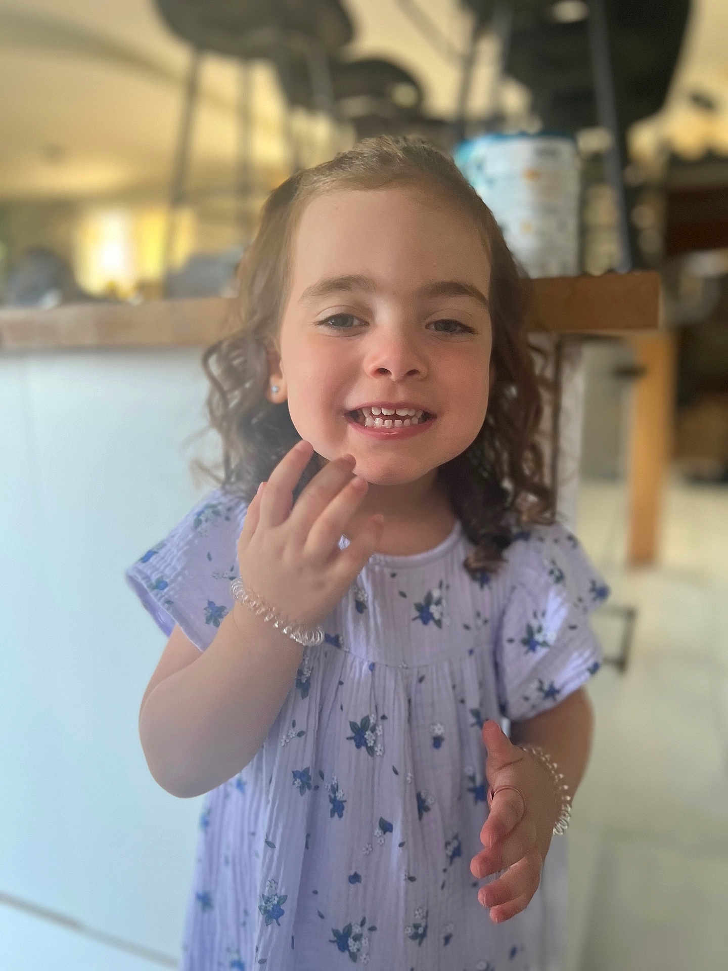 Emy participe au concours pour gagner de l'argent avec cette photo : child, girl, smiling, curly_hair, dress, floral_pattern, bracelet, earrings, indoor, kitchen, counter, blurred_background, happy, portrait, person, young, cute, hand, standing, casual