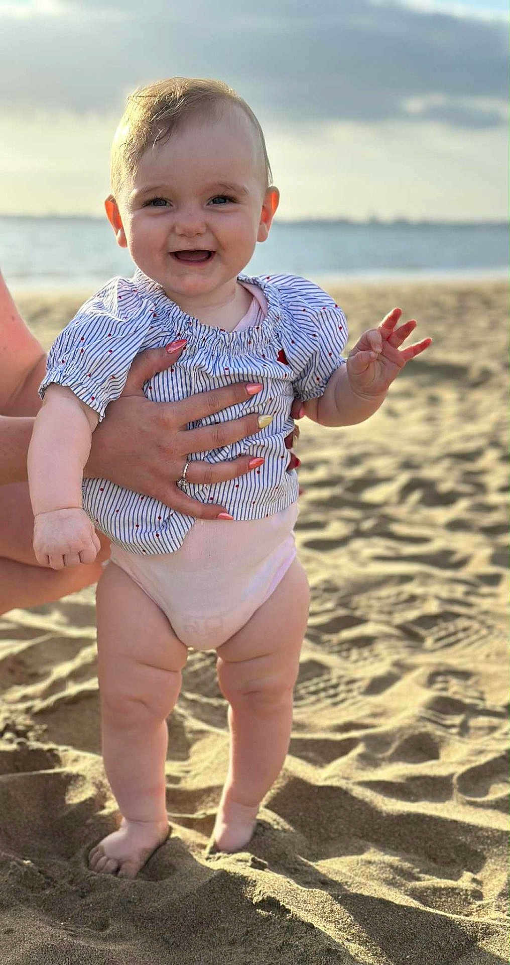 Tessa participe au concours pour gagner de l'argent avec cette photo : baby, child, beach, sand, ocean, smile, happy, person, hand, clothing, diaper, summer, outdoor, sunlight, portrait, cute, support, nail_polish, striped_shirt, feet