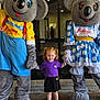 child, girl, redhead, pigtails, mascot, koala_costume, costume, theme_park, dreamworld, holding_hands, polka_dot_dress, purple_shirt, black_skirt, purple_shoes, sidewalk, glass_window, indoor, smiling, photo_op, family_fun