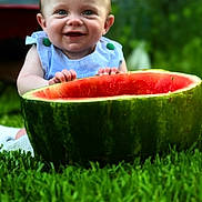 Asher is registered to the contest to win money with this photo: baby, child, watermelon, fruit, grass, outdoor, smiling, happy, nature, green, summer, cute, fresh, playful, portrait, skin, person, head, hands, blue_clothing
