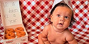 Sanova is registered to the contest to win money with this photo: baby, infant, donuts, krispy_kreme, paper_hat, red_and_white_checkered, blanket, food, box, celebration, half_birthday, cute, chubby, sitting, curly_hair, skin, expression, indoor, portrait, milestone