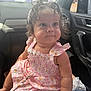 baby, child, curly_hair, pink_dress, floral_pattern, bow, car_interior, seat, cute, smiling, sitting, hand, face, eyes, infant, young_child, clothing, person, indoors, portrait