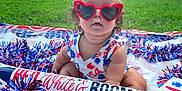Sanova is registered to the contest to win money with this photo: baby, child, sunglasses, heart_shaped, red_bows, patriotic, blanket, outdoor, grass, summer, celebration, red_white_blue, inflatable_rocket, festive, cute, smiling, holiday, fun, person, portrait