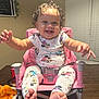 baby, child, smiling, curly_hair, high_chair, pink, pajamas, minnie_mouse, cheese_puffs, table, can, soda, indoor, window_blind, plant, happy, person, foot, hand, face