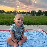 Alejandro joined the competition — help win amazing prizes! baby, barefoot, blanket, casual_clothing, child, clouds, cute, grass, greenery, happy, infant, nature, one_person, outdoor, person, portrait, sitting, sky, smiling, sunset