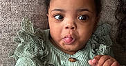 Chloe is registered to the contest to win money with this photo: baby, child, tongue_out, green_clothing, ruffles, couch, texture, hand, face, wide_eyes, infant, cute, lying_down, indoors, portrait, cozy, expression, person, closeup, smiling