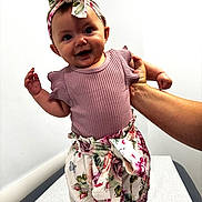 Madalyn joined the competition — help win amazing prizes! baby, child, smiling, headband, floral, clothing, shorts, hand, adult, indoor, white_wall, minimalist, person, cute, happy, portrait, standing, infant, fashion, bright