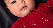 Evelynn is registered to the contest to win money with this photo: baby, infant, child, portrait, close_up, lying_down, red_onesie, star_pattern, dark_blanket, face, eyes, wide_eyed, smiling, fist, hand, indoor, cozy, cute, photography, textile