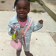 Nala is registered to the contest to win money with this photo: child, girl, smiling, juice_box, denim_jacket, pink_purse, hair_beads, bows, sidewalk, sneakers, shorts, pink_socks, casual_clothing, outdoor, happy, posing, person, accessories, cute, playful
