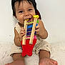 baby, child, toy, wooden_toy, cap, black_cap, smiling, cute, playing, sitting, barefoot, bracelet, colorful, indoor, white_background, happy, infant, chewing, clothing, person