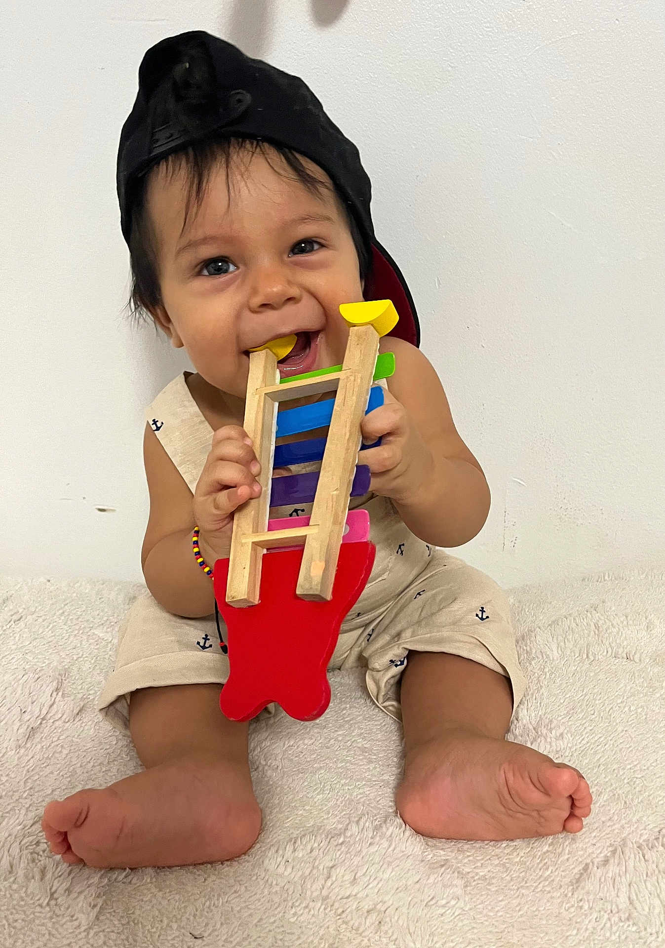 Nicolas joined the competition — help win amazing prizes! baby, child, toy, wooden_toy, cap, black_cap, smiling, cute, playing, sitting, barefoot, bracelet, colorful, indoor, white_background, happy, infant, chewing, clothing, person
