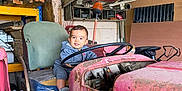 Jules a rejoint le concours — aidez-le/la à gagner de superbes lots ! toddler, child, tractor, steering_wheel, shed, rusty, old_vehicle, wooden_planks, tools, cluttered, smiling, indoor, seat, clothing, face, person, machine, metal, gray_hoodie, floor