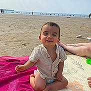 Jules a rejoint le concours — aidez-le/la à gagner de superbes lots ! toddler, child, beach, sand, ocean, towel, mat, smile, shirt, diaper, sunny, relaxed, person, legs, water, outdoor, happy, vacation, summer, playtime