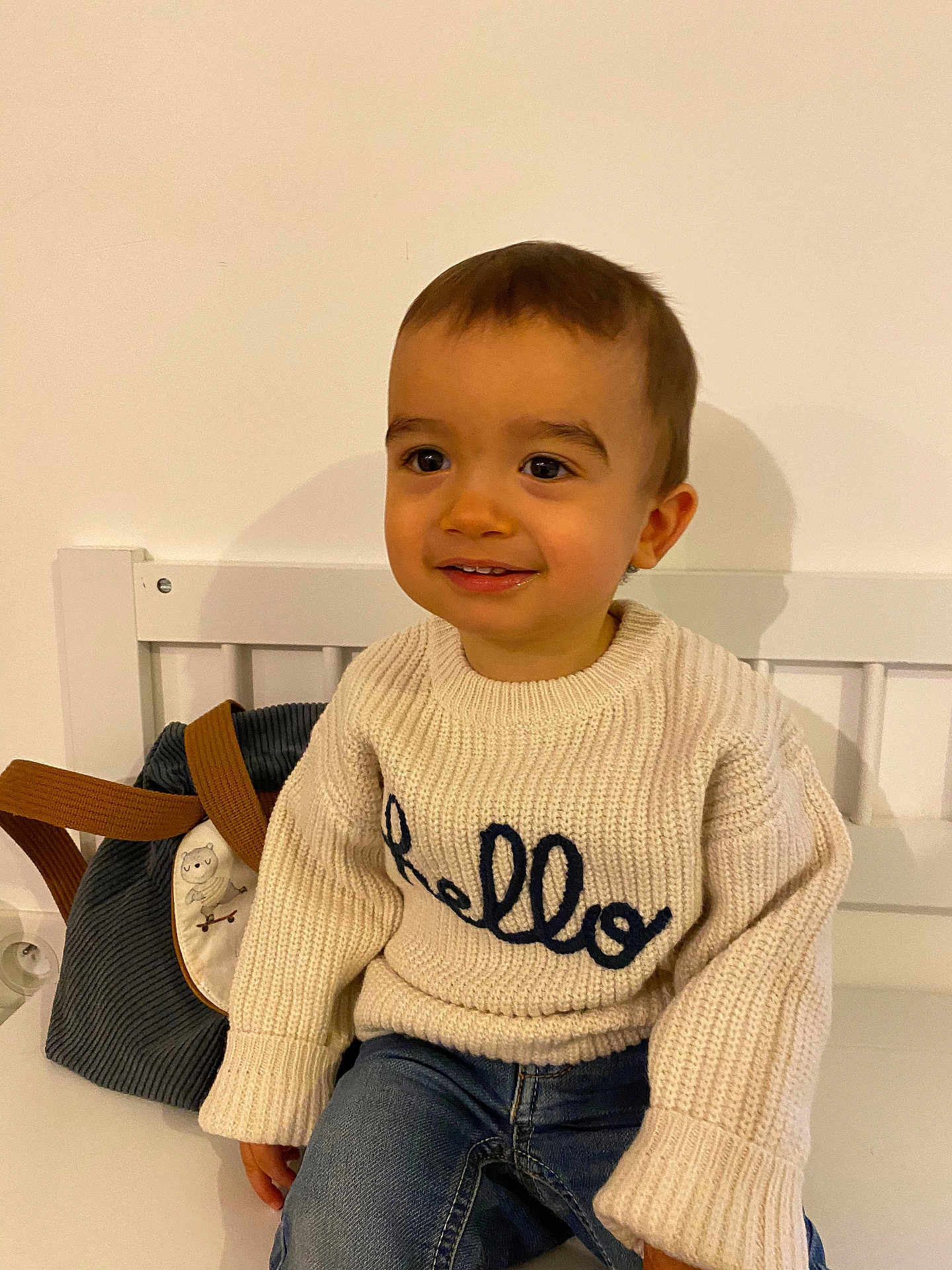 Jules a rejoint le concours — aidez-le/la à gagner de superbes lots ! toddler, child, smiling, sweater, knitwear, jeans, bench, backpack, indoor, portrait, happy, cute, young_child, casual_clothing, seated, person, face, head, warm_clothing, cozy