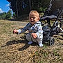 Ethan participe au concours pour gagner de l'argent avec cette photo : toddler, child, outdoor, grass, stroller, sunlight, forest, nature, happy, exploring, smiling, casual_clothing, daytime, trees, pathway, shadows, socks, playful, baby, curious