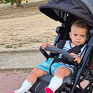 Ethan a rejoint le concours — aidez-le/la à gagner de superbes lots ! toddler, child, stroller, outdoor, park, trees, grass, sidewalk, clothing, socks, expression, face, seatbelt, summer, playground, person, baby, casual, sunlight, nature