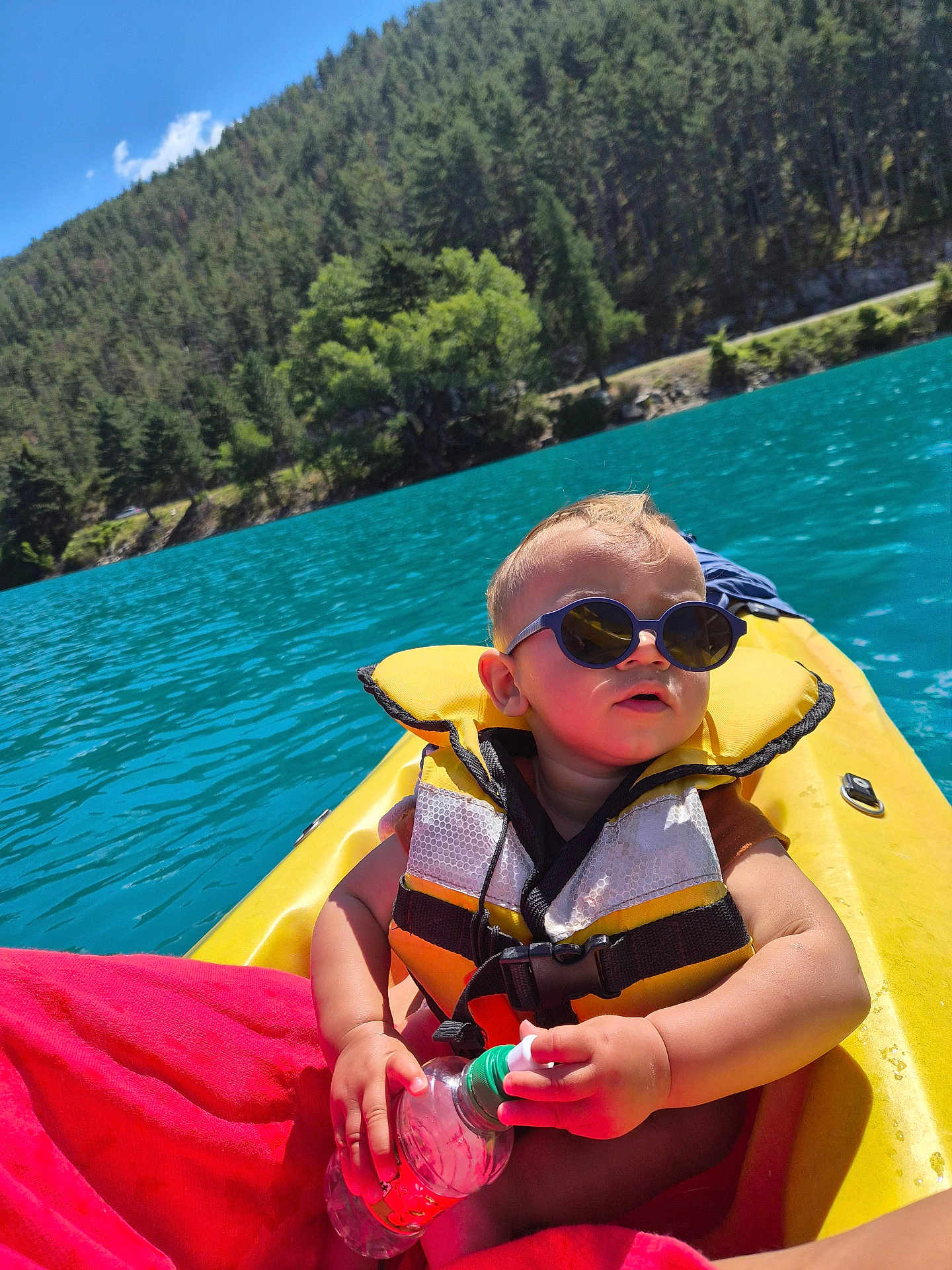 Ethan participe au concours pour gagner de l'argent avec cette photo : baby, sunglasses, life_jacket, kayak, water_bottle, lake, forest, water, outdoor, sunny, child, nature, summer, adventure, person, recreation, greenery, sky, trees, vacation