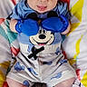 baby, infant, child, portrait, lying_down, sitting, blue_gloves, boxing_gloves, mickey_mouse, cartoon, romper, socks, blanket, colorful, geometric_pattern, playful, tongue_out, indoor, close_up, happy
