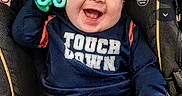 Enzo joined the competition — help win amazing prizes! baby, blue_shirt, car_seat, child, close_up, clothing, face, green_toy, happy, head, indoors, infant, laughing, orange_pants, portrait, single_person, sitting, smiling, toy, vehicle