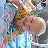 baby, child, smiling, happy, playpen, infant, portrait, indoor, blanket, toy, colorful, seated, lying_down, blond_hair, clothing, nursery, bed, play_area, smartphone_screenshot, social_media