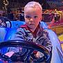 Liam participe au concours pour gagner de l'argent avec cette photo : child, toddler, steering_wheel, amusement_park, ride, blue_car, night, lights, denim_jacket, playground, fun, outdoor, person, carnival, colorful, young, toy_car, seat, entertainment, event
