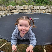 Ana Matilda a rejoint le concours — aidez-le/la à gagner de superbes lots ! child, pigtails, tongue_out, trampoline, playful, springs, gray_sweatshirt, outdoor, grass, stone_wall, smiling, happy, young_child, person, fun, nature, expression, tongue, holding, casual_clothing