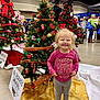 Riley is registered to the contest to win money with this photo: child, christmas_tree, clothing, event, family, festive, floor, gold_decor, happy, holiday_decorations, indoor, market, ornaments, people, person, red_ribbon, shopping, smiling, sneakers, toddler