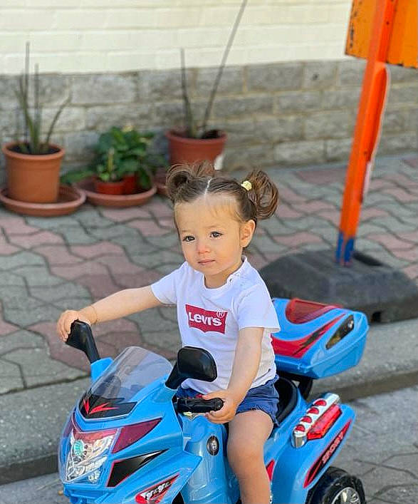 Lina participe au concours pour gagner de l'argent avec cette photo : automotive_design, automotive_exterior, automotive_lighting, automotive_tire, blue, fender, flowerpot, grass, happy, houseplant, motor_vehicle, person, plant, public_space, riding_toy, summer, tire, toddler, toy, vehicle