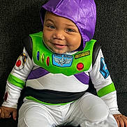 Silas is registered to the contest to win money with this photo: baby, child, costume, buzz_lightyear, purple_hood, smile, face, sitting, couch, clothing, green, white, black, indoor, cute, portrait, happy, infant, person, young