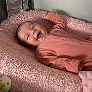Anna is registered to the contest to win money with this photo: baby, infant, smiling, onesie, pink_blanket, playpen, pacifier, happy, cute, child, newborn, soft_texture, sleepwear, lying_down, indoor, face, skin, hand, cheerful, cozy