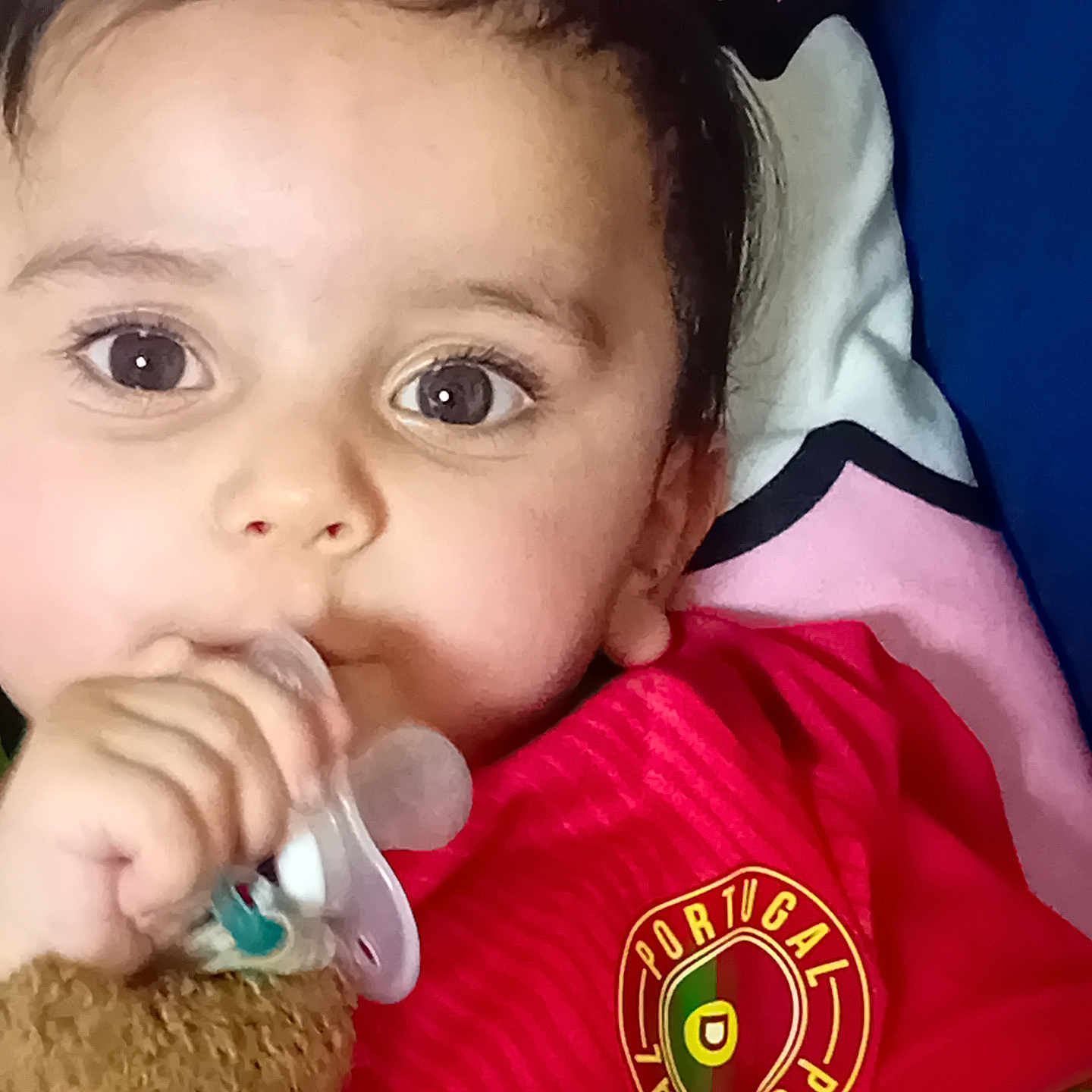 Mehdi participe au concours pour gagner de l'argent avec cette photo : baby, blanket, child, close_up, colorful, cute, expression, face, hand, indoors, infant, pacifier, person, portrait, portugal_jersey, red_shirt, sleepwear, soft_toy, teddy_bear, young_child