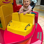 Cassian joined the competition — help win amazing prizes! toddler, child, smiling, indoor, kiddie_ride, toy, boat, yellow, pink, stroller, striped_shirt, happy, playful, floor_tiles, hands, face, hair, person, amusement, fun