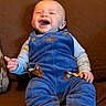 baby, child, laughing, smiling, blue_overalls, gray_shirt, couch, brown_couch, quilted, happy, infant, person, seated, indoors, cute, young_child, footwear, orange_soled_shoes, portrait, comfortable