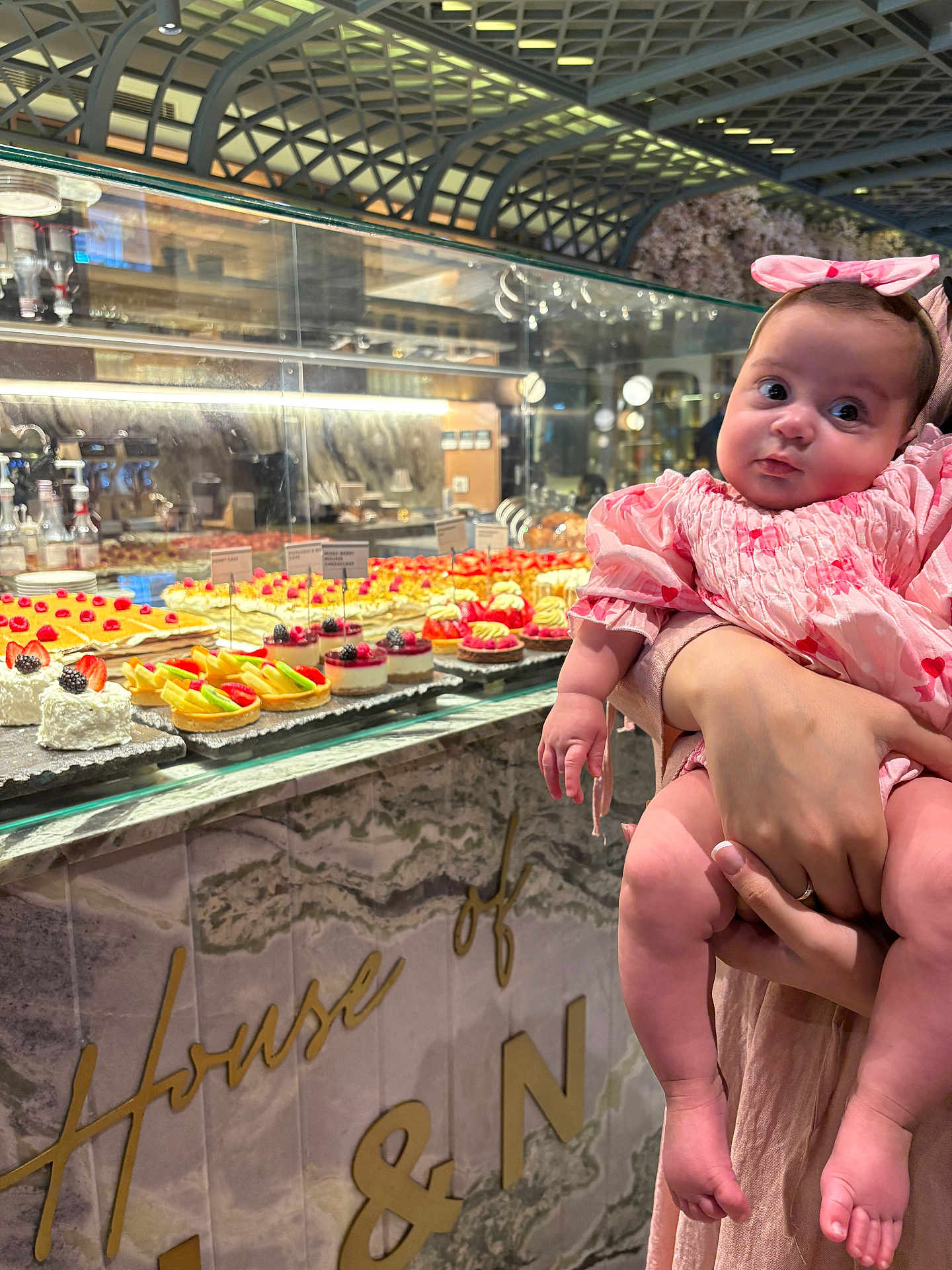 Talene is registered to the contest to win money with this photo: baby, child, pink_clothing, bow, desserts, cakes, bakery, glass_display, marble_counter, hand, person, indoor, food, sweet, pastry, fruit, blackberry, strawberry, curious, cute