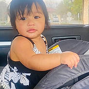 Elelkihda is registered to the contest to win money with this photo: baby, black_hair, car_interior, car_seat, child, cute, daylight, expression, face, floral_dress, hand, indoors, looking_away, person, portrait, seatbelt, sitting, toddler, window, young_child