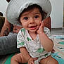 baby, child, hat, smile, dinosaur_print, tshirt, play_mat, indoor, adult, glasses, tattoo, happy, sitting, hand_on_face, floor, person, cute, family, joyful, portrait