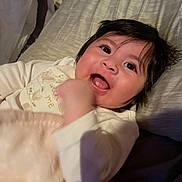 Skyler is registered to the contest to win money with this photo: baby, infant, child, smile, happy, plush_toy, bed, blanket, pillow, clothing, face, dark_hair, open_mouth, cute, indoors, closeup, portrait, lying_down, soft_toy, cozy