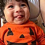 baby, child, infant, orange_shirt, pumpkin_face, tongue_out, smiling, person, cute, happy, indoors, adult, white_tank_top, face, hair, skin, hand, clothing, holding, closeup