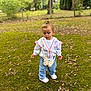 toddler, child, outdoor, park, grass, moss, trees, casual_clothing, white_shoes, butterfly_purse, curly_hair, nature, fall_leaves, greenery, young_child, standing, daylight, cute, casual, curious