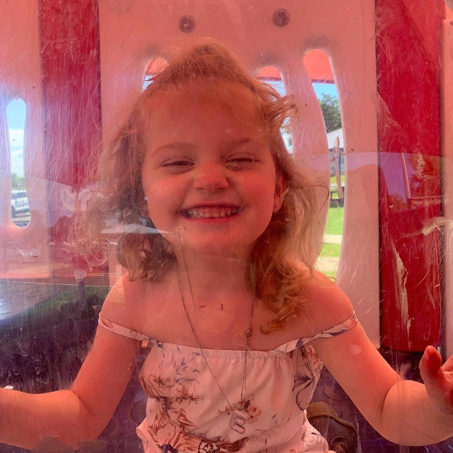 Emily joined the competition — help win amazing prizes! child, colorful, curly_hair, face, floral_dress, girl, happy, joy, necklace, outdoor, person, plastic_window, play, playground, portrait, reflection, scratches, smiling, summer, sunlight